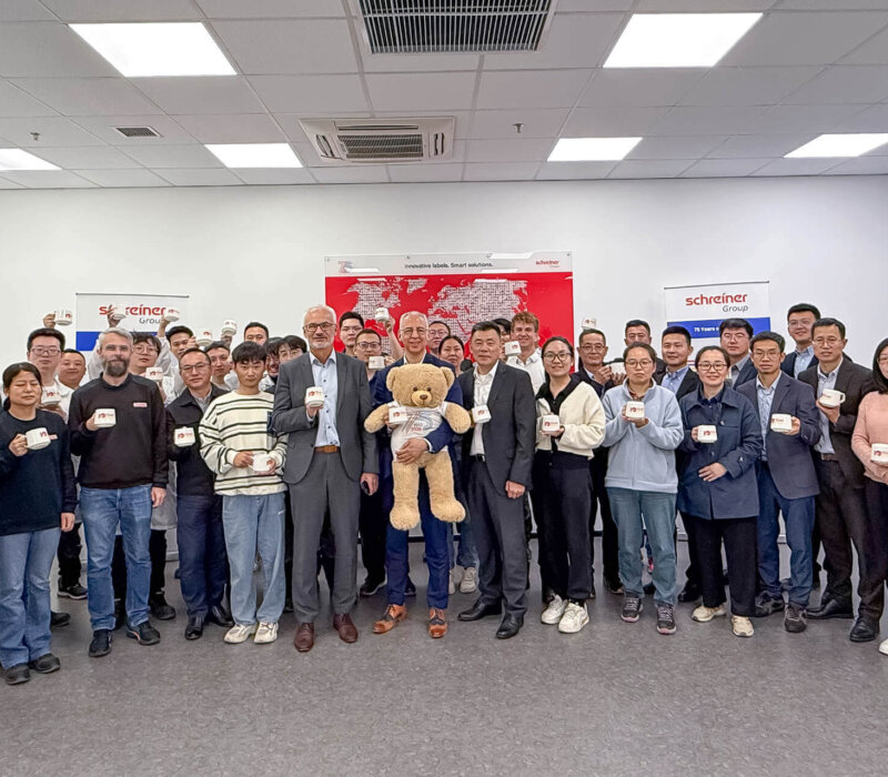 The workforce of Schreiner Group’s Chinese site celebrates the 10th anniversary together with Roland Schreiner (with the anniversary mascot “Bärli”) and Thomas Köberlein.