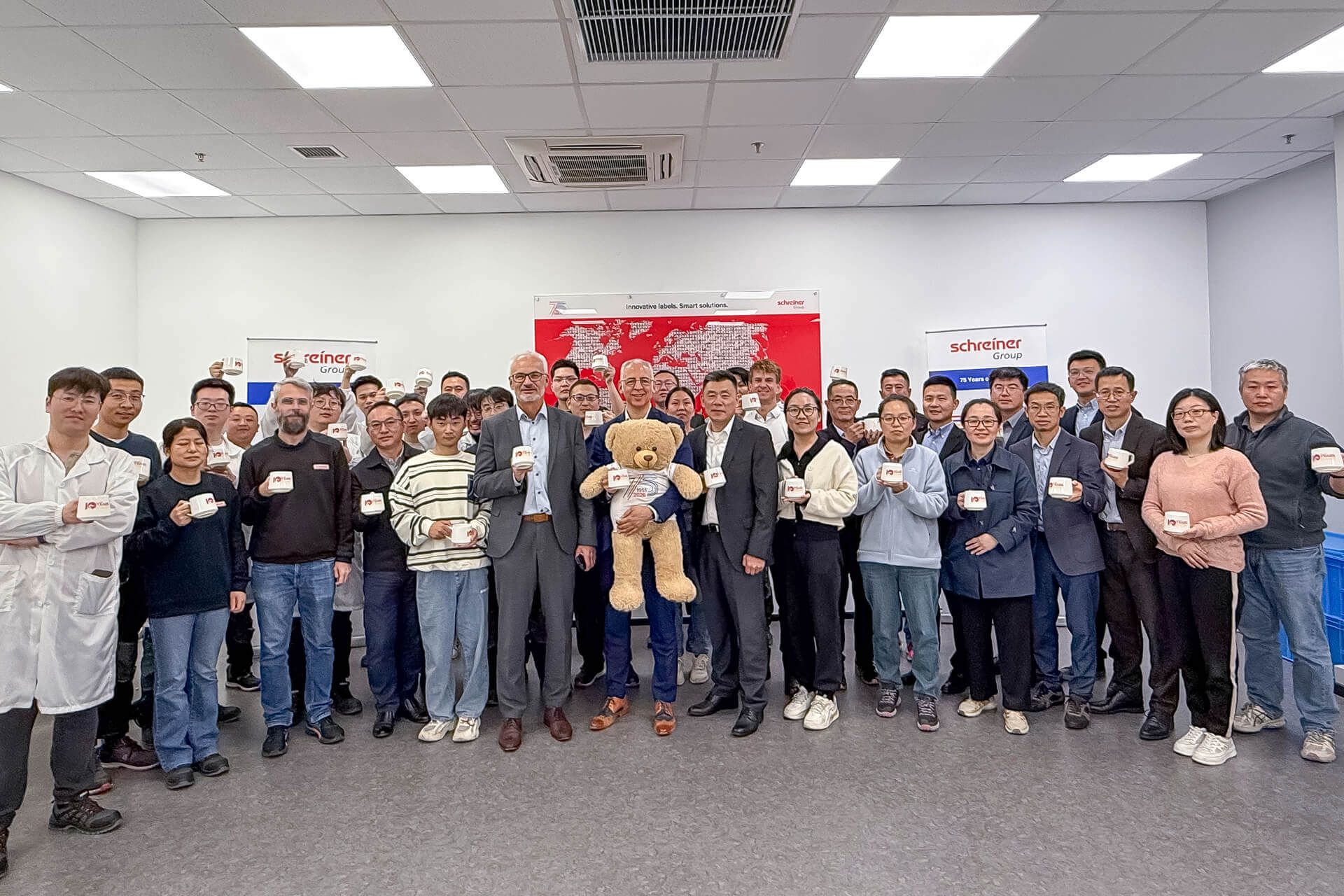 The workforce of Schreiner Group’s Chinese site celebrates the 10th anniversary together with Roland Schreiner (with the anniversary mascot “Bärli”) and Thomas Köberlein.